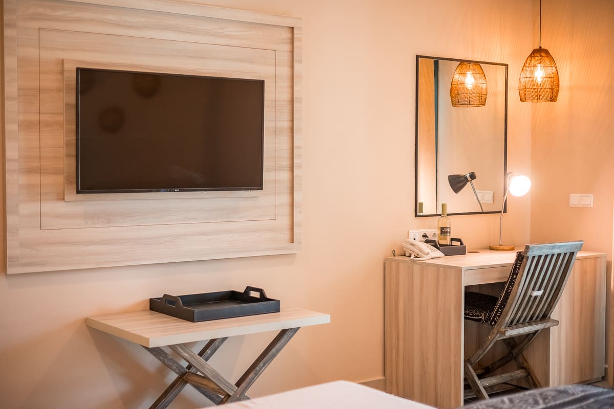 Guest room desk area at Bakadaji Hotel with wall-mounted television, mirror, fitted desk and pendant lighting