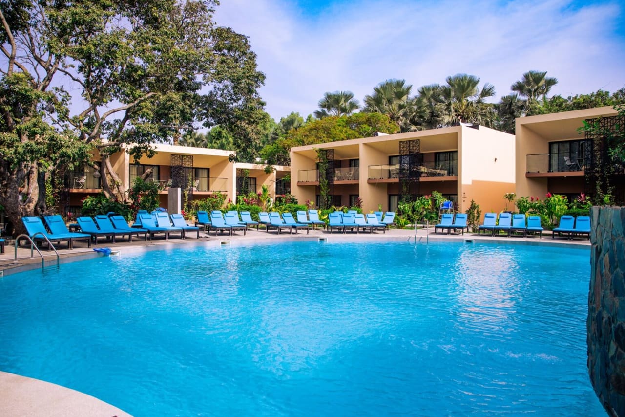 Swimming pool at Bakadaji Hotel lined with sun loungers, with two-storey guest room blocks and mature trees behind