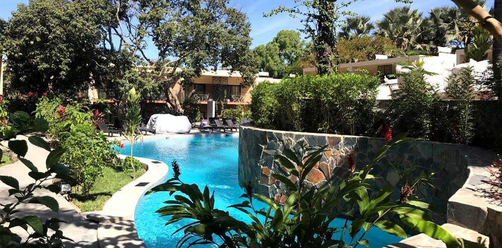 Curved pool edge at Bakadaji Hotel framed by stone-clad retaining walls and dense tropical planting