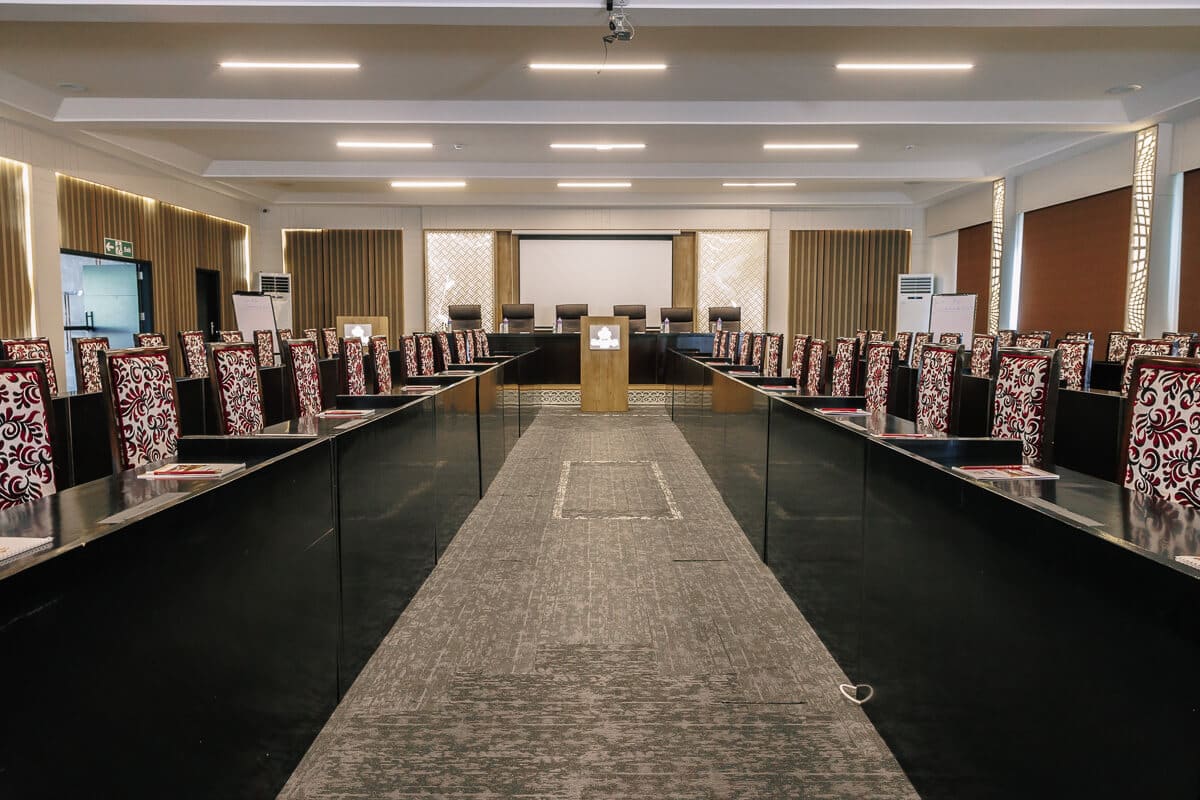 Conference hall at Bakadaji Hotel set out boardroom style with patterned chairs, projection screen and lectern