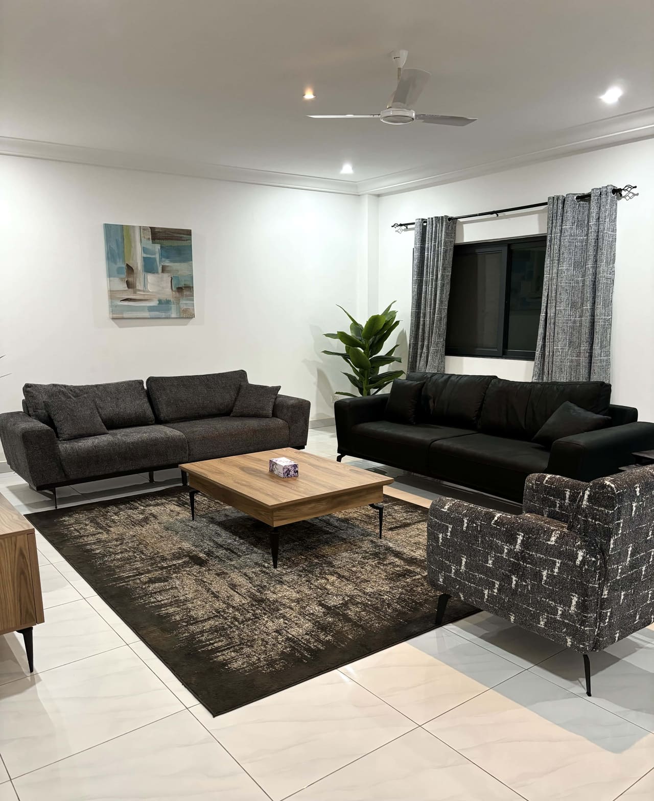 Furnished sitting room in a Fajara Lux apartment with large-format floor tiling, ceiling fan and curtained window