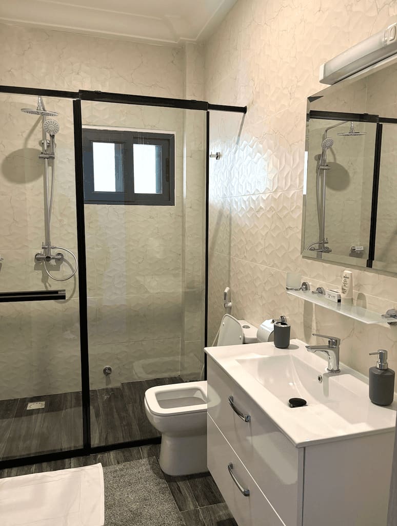 En-suite bathroom at Fajara Lux with walk-in glass shower enclosure, textured wall tiling and fitted vanity unit