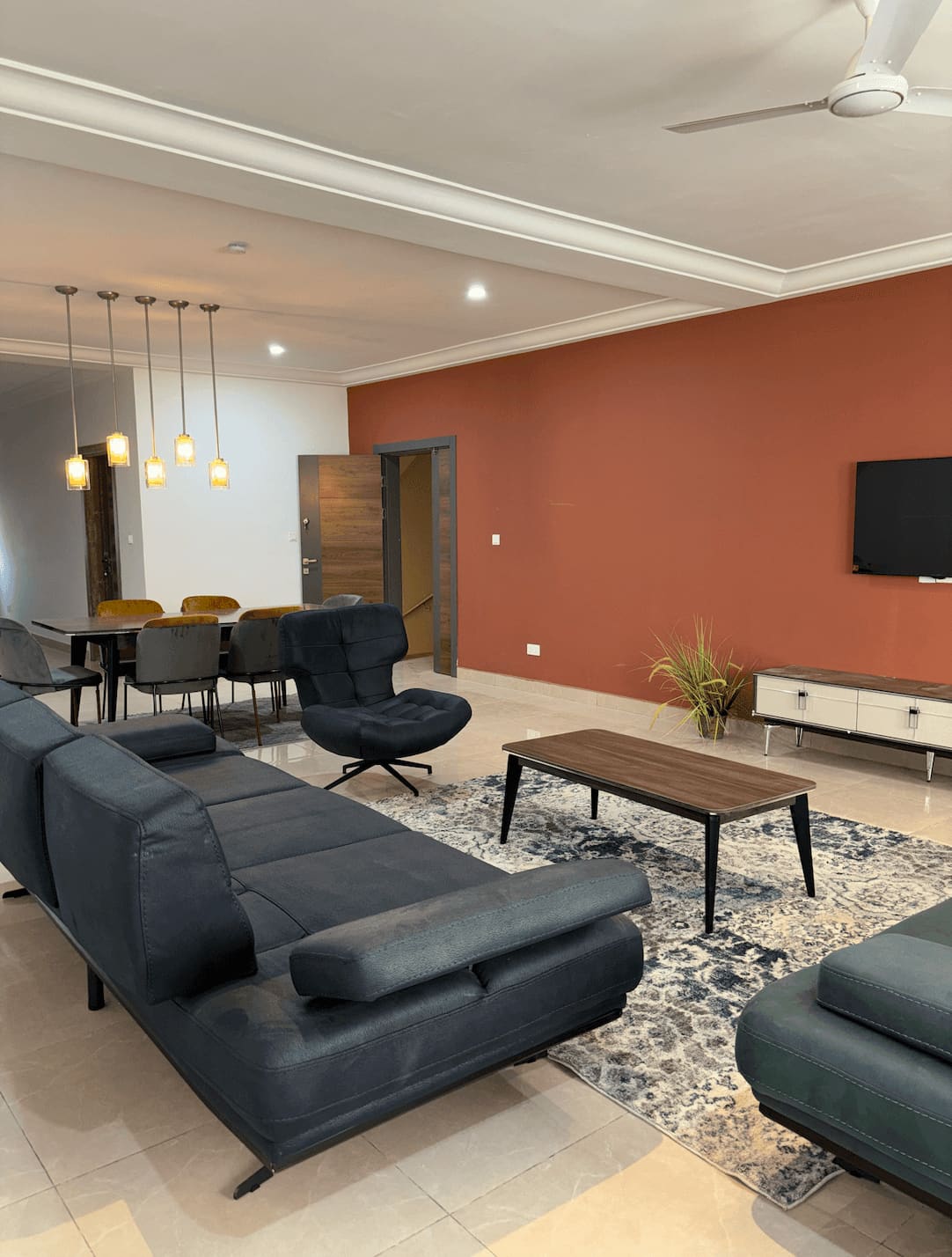 Open-plan living and dining room in a Fajara Lux apartment with terracotta accent wall, dropped ceiling and pendant lighting