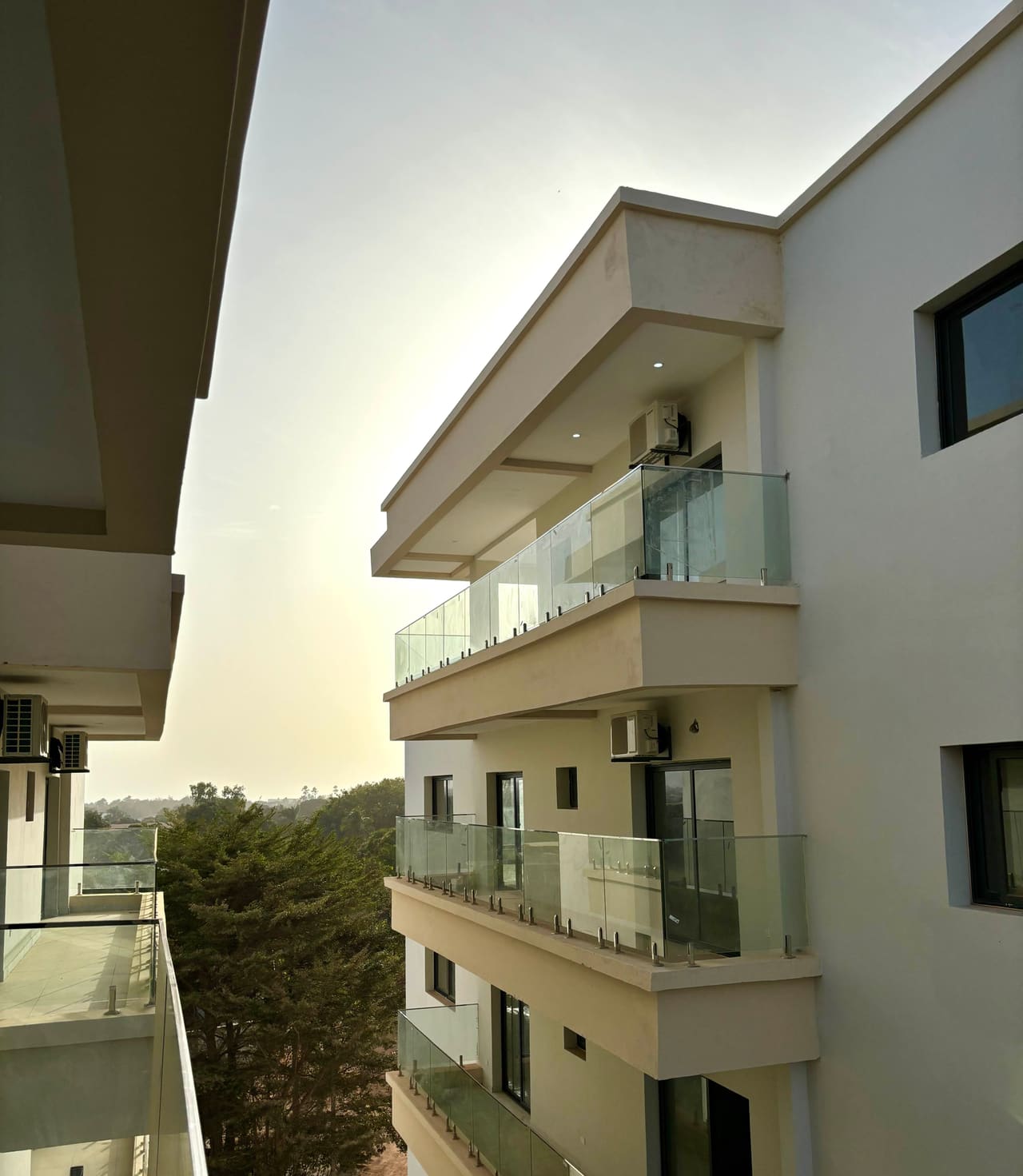 View along the Fajara Lux balconies from an upper floor, with glass balustrades and treetops beyond